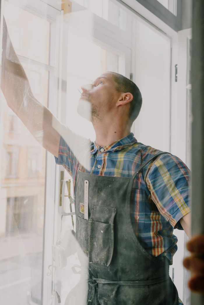 Mastering the First Impression: Your intriguing post title goes here Professional focused craftsman in uniform standing with raised arm standing behind glass while assembling window in apartment during renovation works