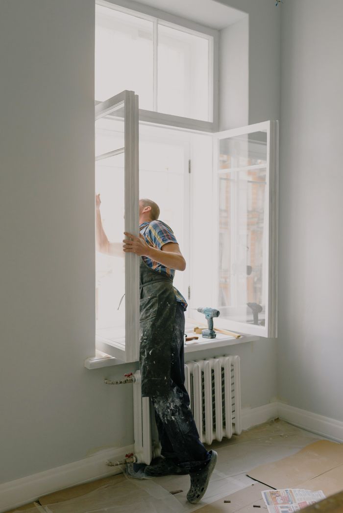 Hello world! Side view of anonymous handyman in uniform mounting window frame during renovation process in flat