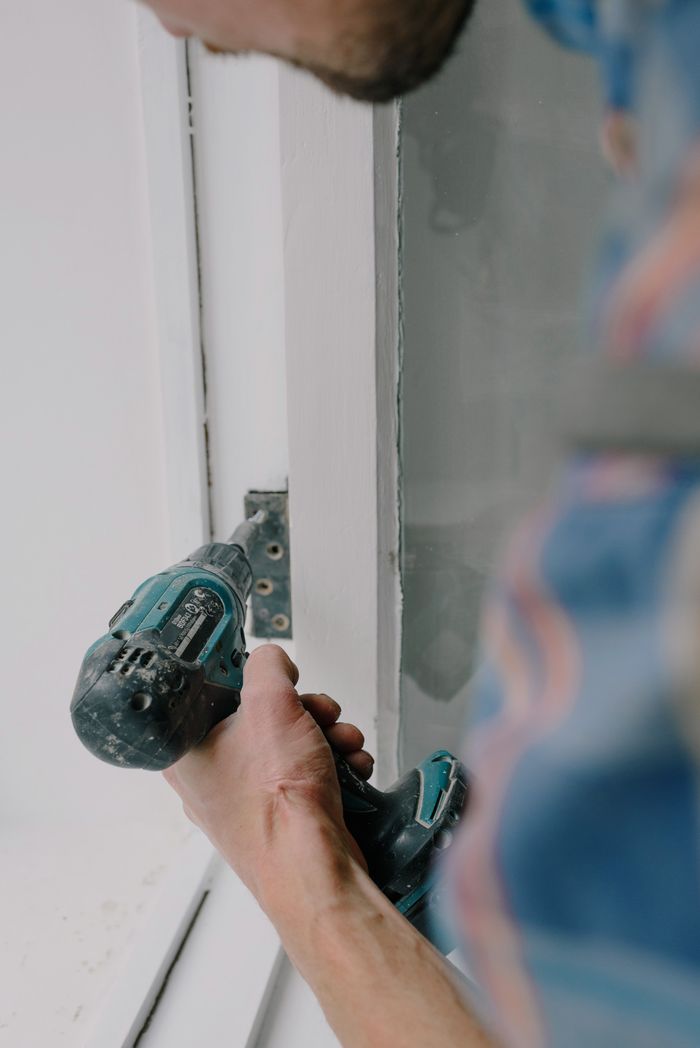 Home Crop bearded guy installing new wooden window with contemporary screwdriver and metal hinge during renovation process in apartment